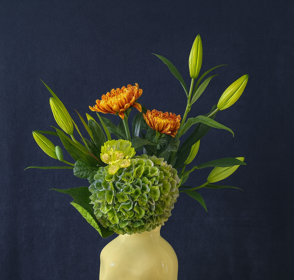 Floral arrangement with large green hydrangea, yellow carnation, orange chrysanthemums, yellow lillies in a yellow hand sculpted vase on a dark background